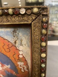 A Tibetan thangka in inlaid gilt brass frame, 19th C.